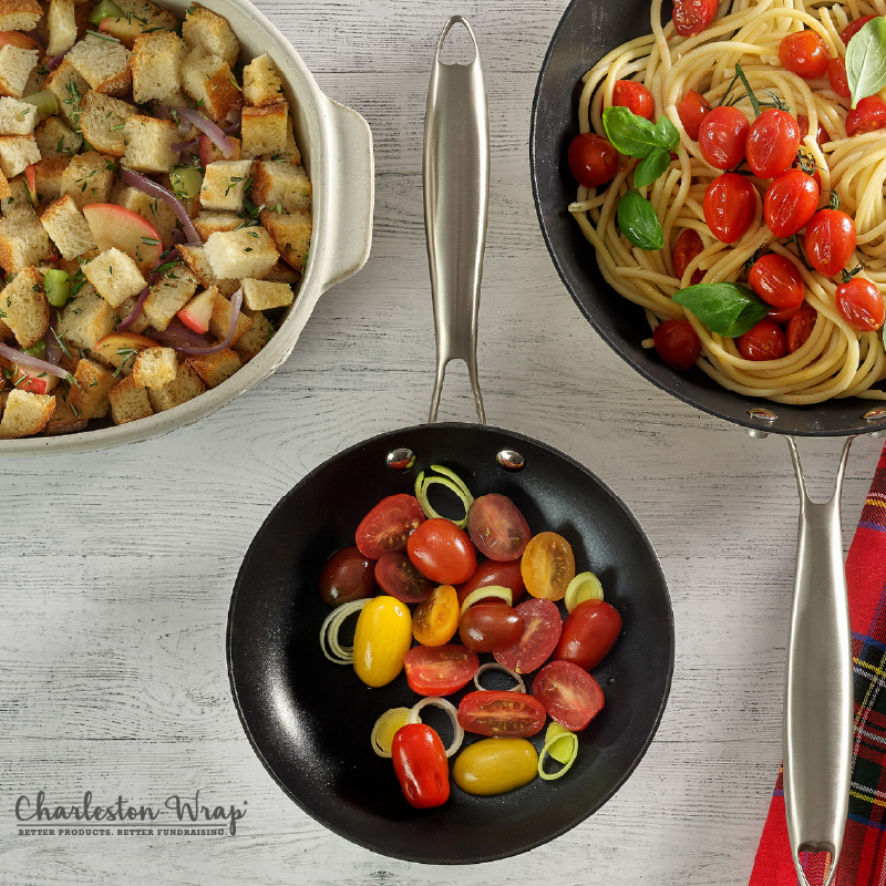 Two pans filled with pasta and tomatoes, accompanied by a loaf of bread on a wooden surface.