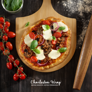 A freshly baked pizza on a wooden cutting board, garnished with ripe tomatoes and fresh basil leaves.